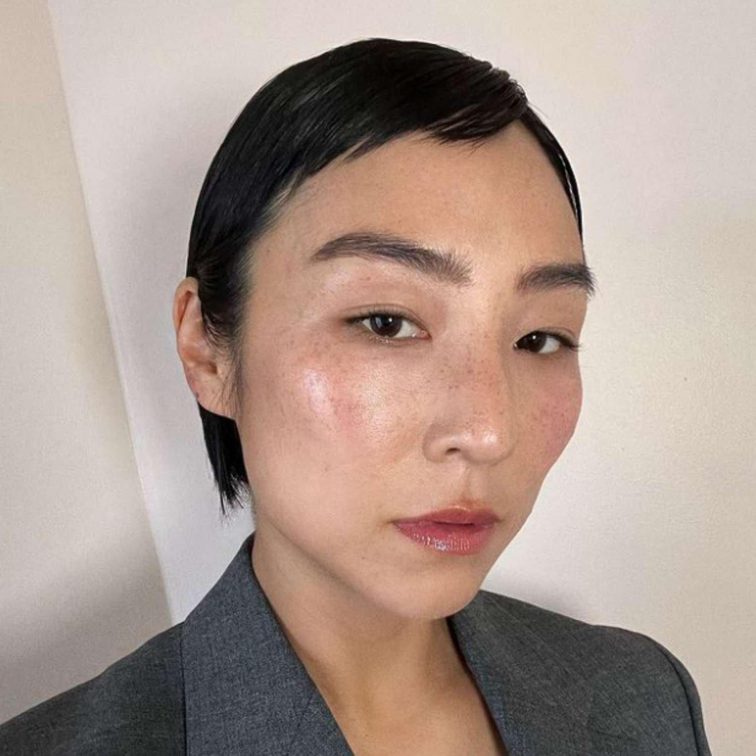 Greta Lee with a blue-black side-swept pixie cut.