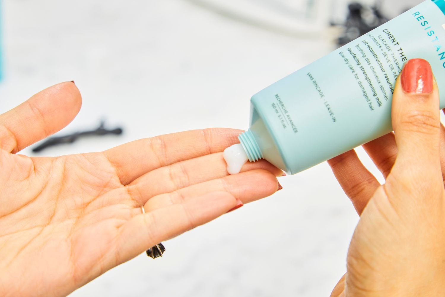 A hand squeezes Kérastase Resistance Ciment Thermique Blow Dry Primer onto fingers