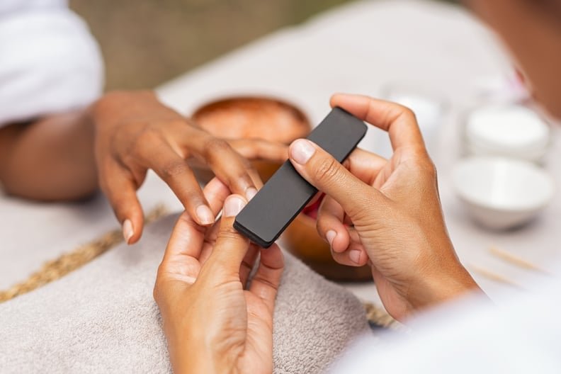 Close up of african hands of a qualified manicurist filing the nails of a young woman. Hands during manicure care session. Detail of a girl in a nail salon receiving manicure.